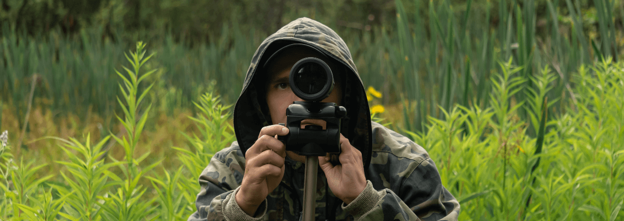 Ein Mann nutzt ein Spektiv zur Vogelbeobachtung in Tarnkleidung.